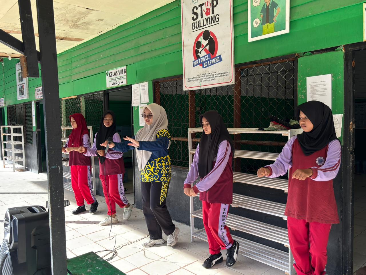 Ustadzah Khairunnisa, S.Pd memimpin gerakan senam bersama beberapa siswa di depan kelas VIII B